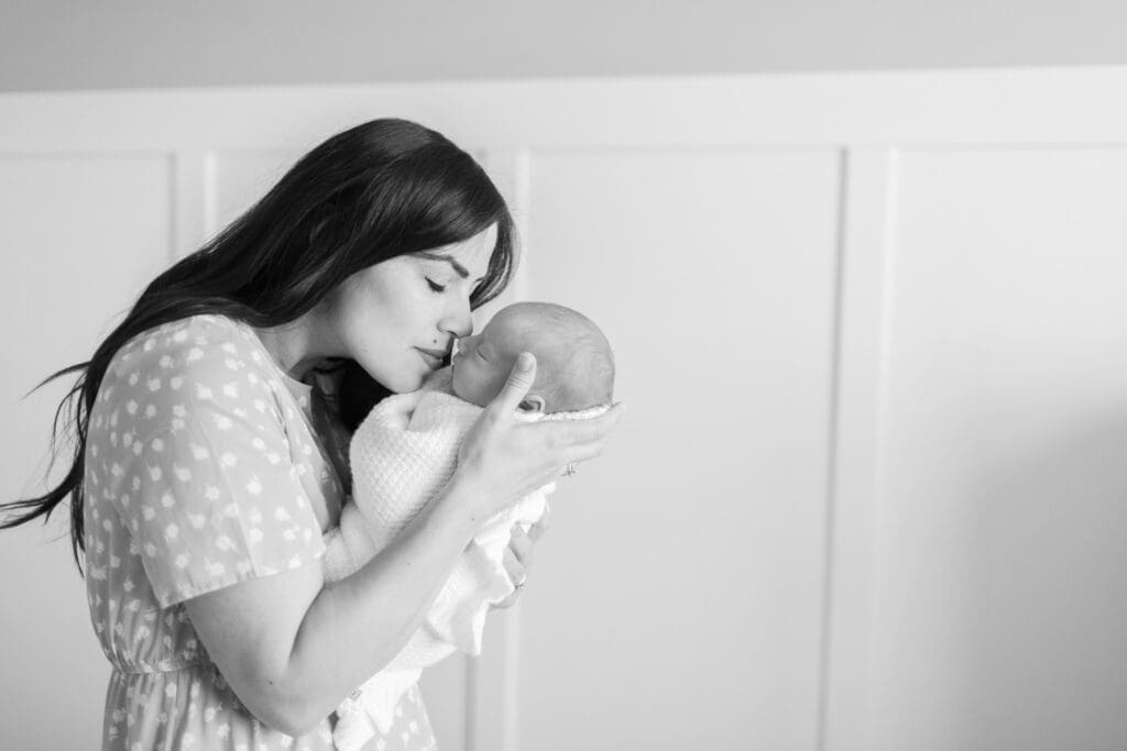 Mother in her master bedroom, touching noses with her newborn during an in-home lifestyle newborn session in South Jordan, Utah