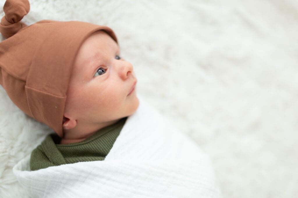 Wide-eyed newborn swaddled and resting on the master bed during an in-home lifestyle newborn session in Highland, Utah