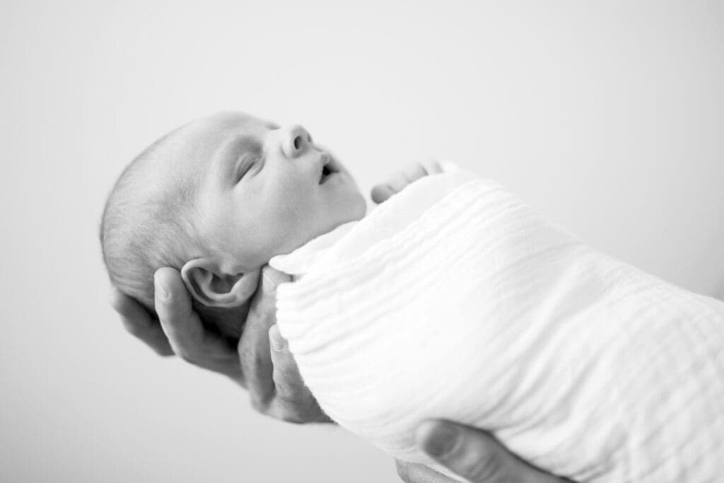 Close-up of a newborn’s profile while being gently held in their dad’s hands during a calm, in-home lifestyle newborn session in South Jordan, Utah.