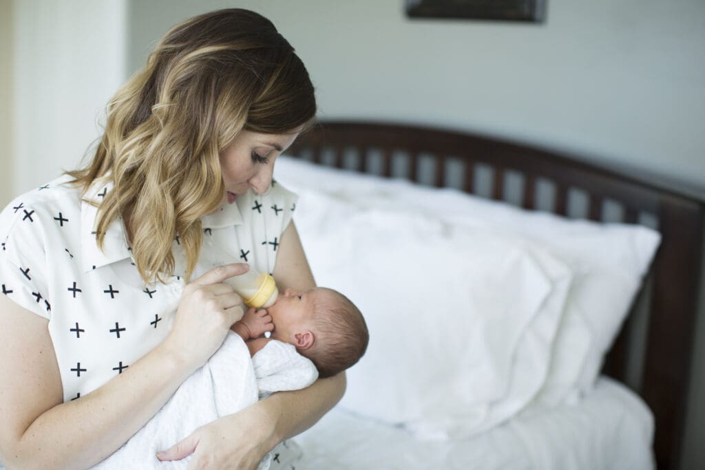 Mother cradling and bottle-feeding her newborn during a natural in-home photography session in South Jordan, Utah