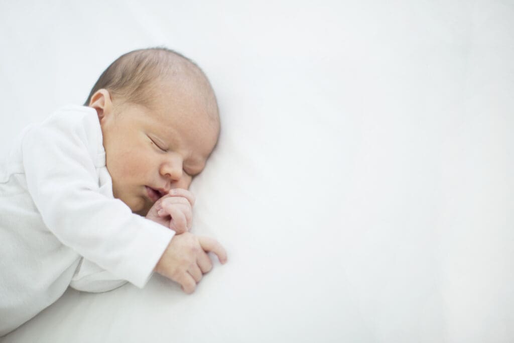 Newborn sleeping peacefully on the master bed during a natural light in-home session in South Jordan, Utah.