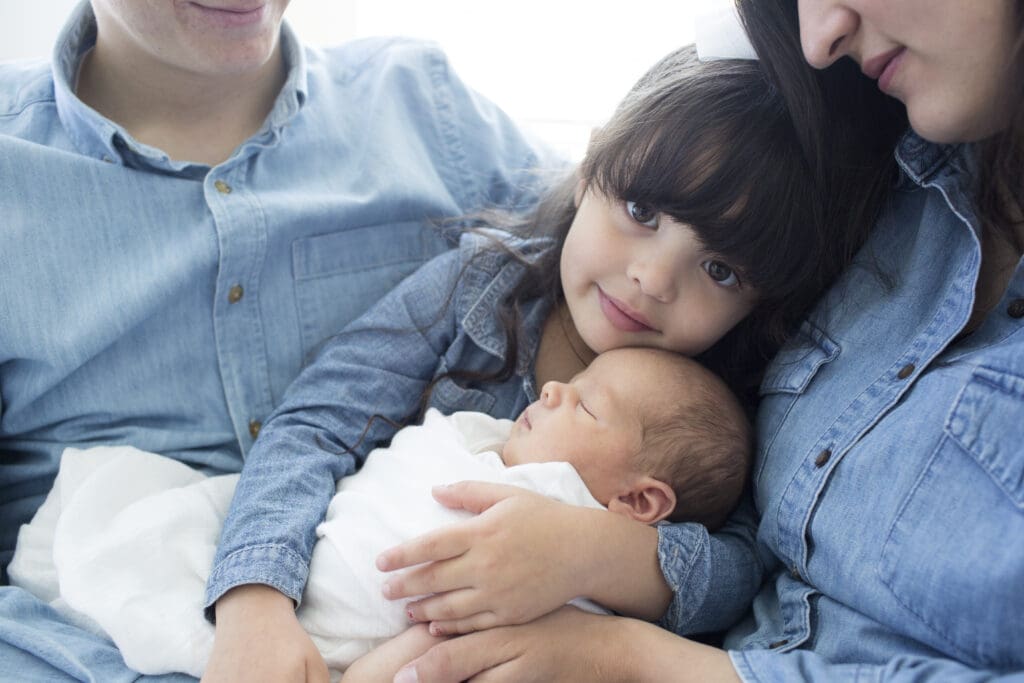 Big sister holding newborn baby brother, surrounded by parents during a calm South Jordan, Utah in-home session
