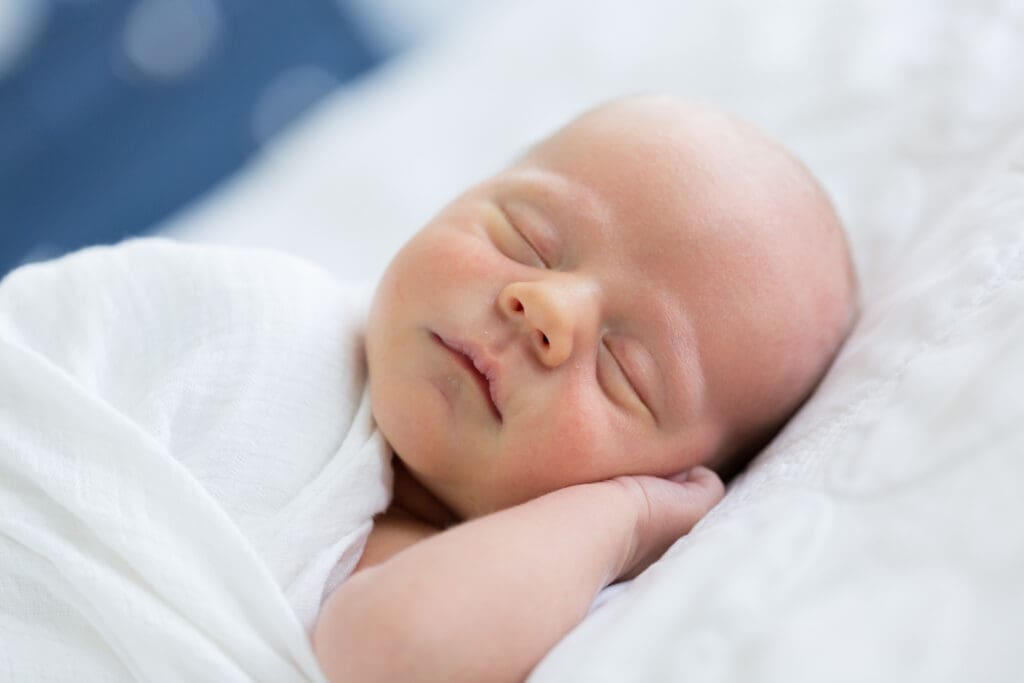 Close-up of a swaddled newborn resting on the master bed during an in-home lifestyle newborn session with a Salt Lake newborn photographer.