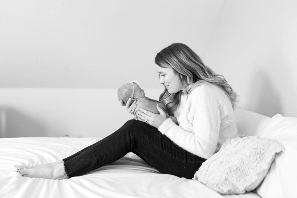 Black and white photo of a mother on her master bed gently holding her newborn close, their faces nearly touching in a tender, nose-to-nose moment.